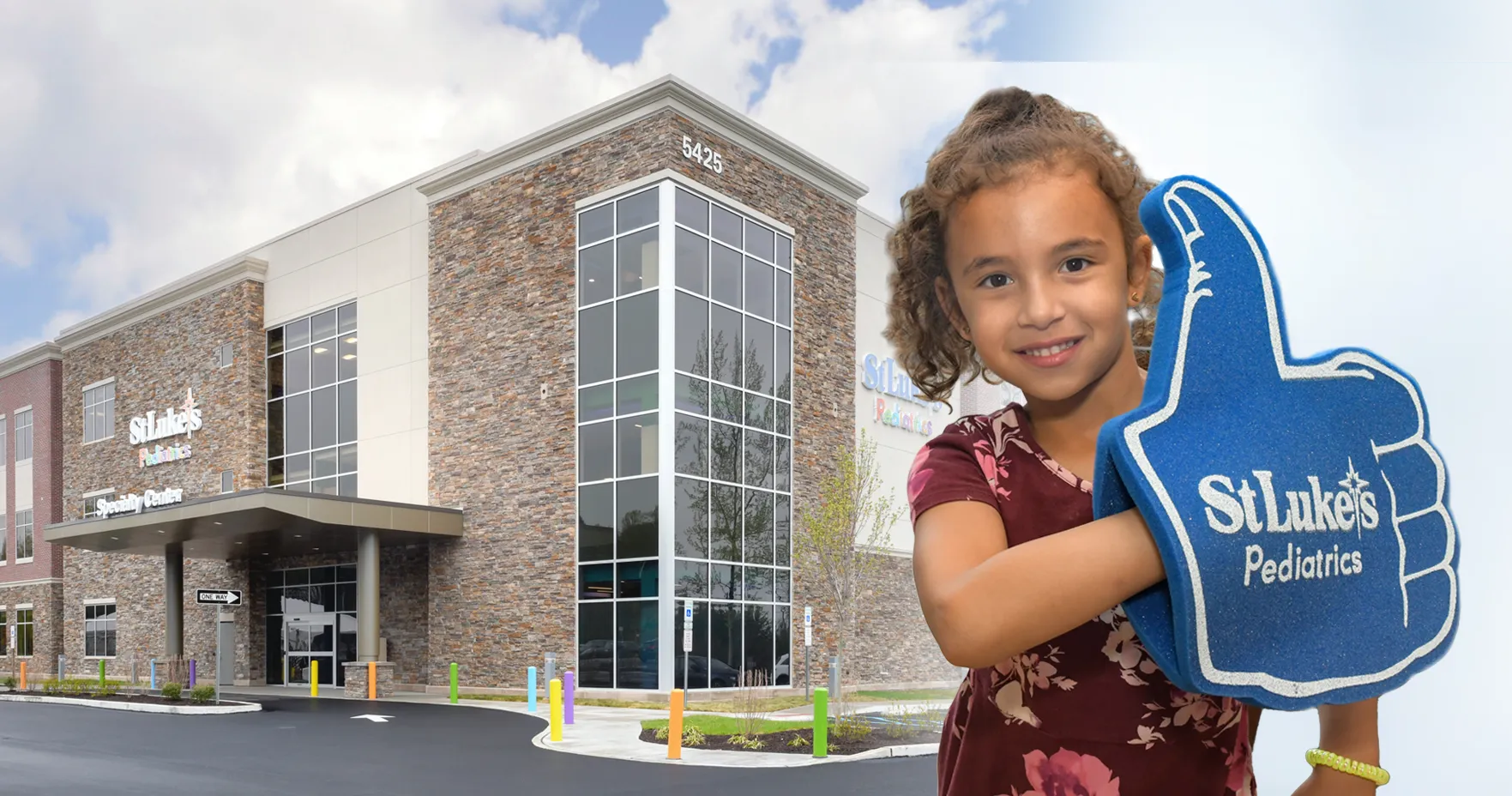 Young girl holding blue thumbs up foam hand while standing in front of a building