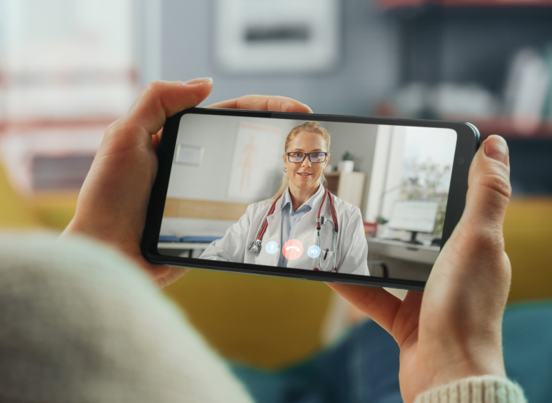 Patient holding up a mobile device with a medical professional on the screen
