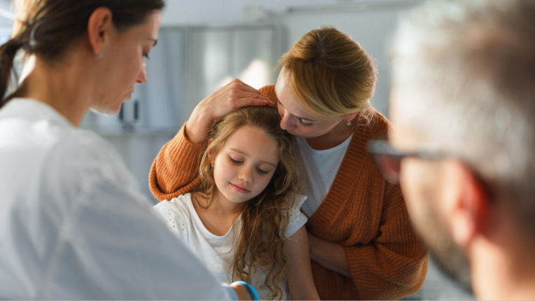 Mother holding her young daughter while talking with medical professionals