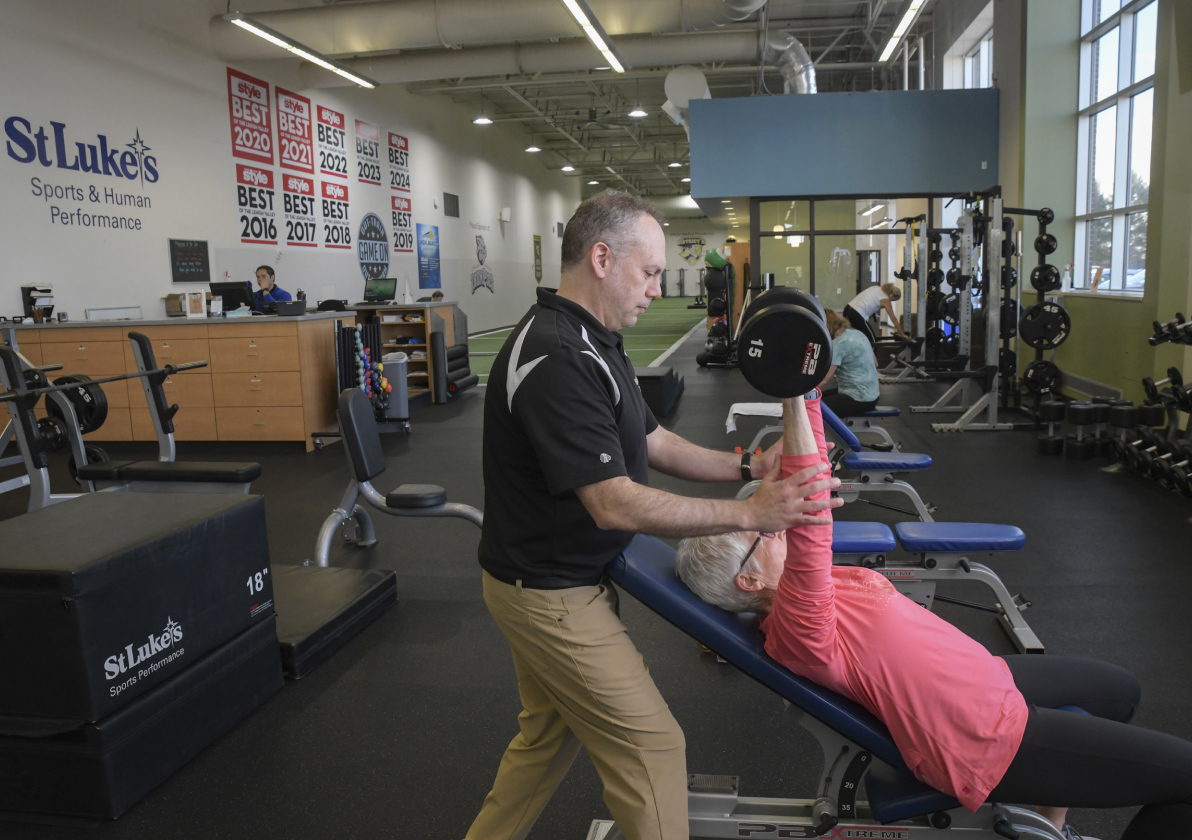 Gym coach assisting a gym member lifting weights on an incline bench