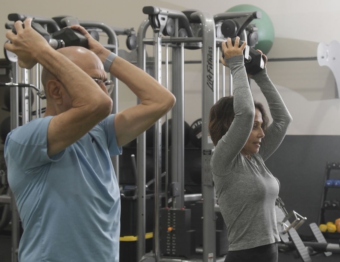Two gym members working out together with dumbbells
