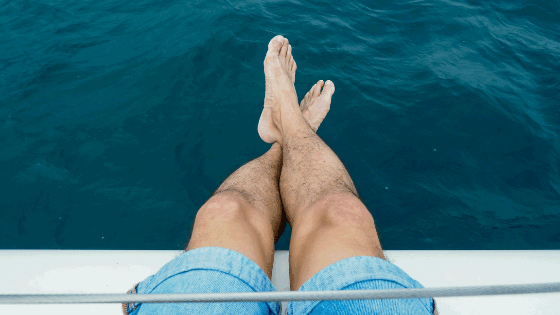 Individual sitting on the edge of a boat with feet in the water