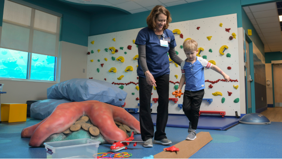 Physical therapist with young patient walking on balance beam