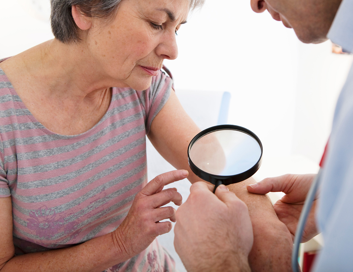 Medical professional looking at a patients arm with a magnify glass