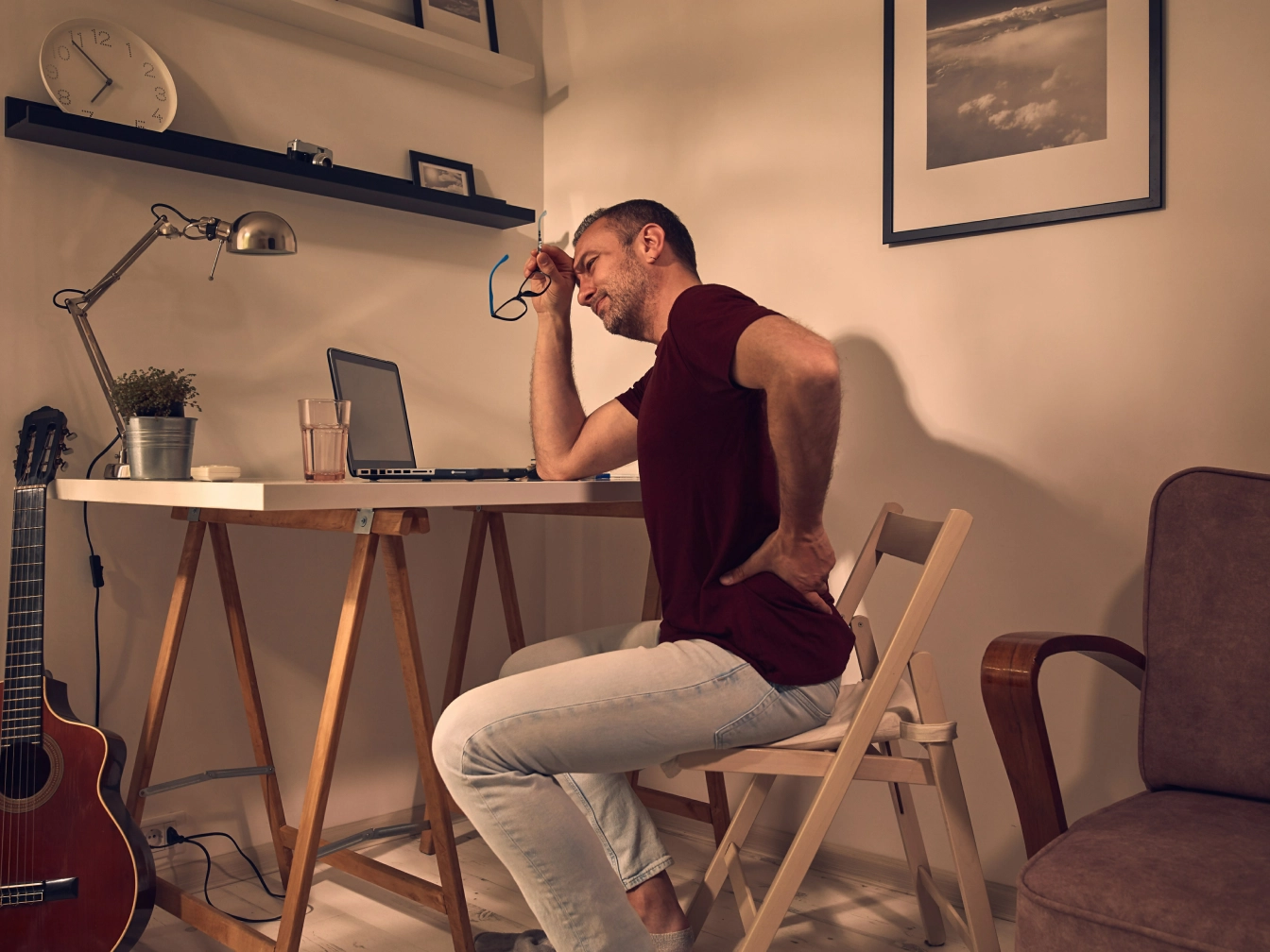 male sitting at a desk holding lower back in pain