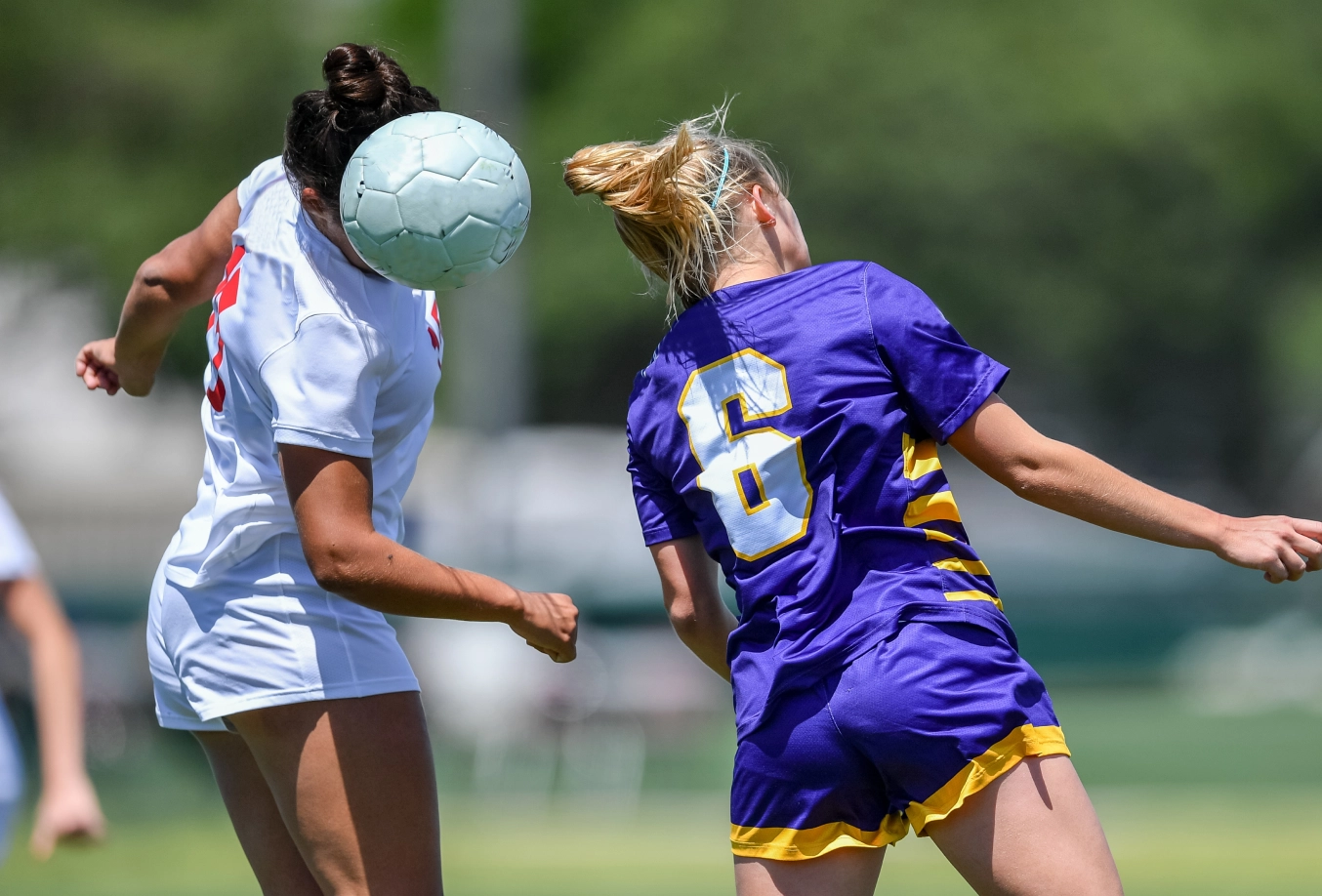 2 female soccer players jumping for soccer ball