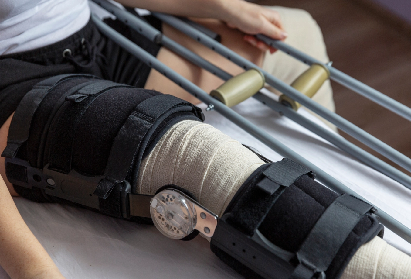 Individual sitting with a knee brace on right knee and holding crutches