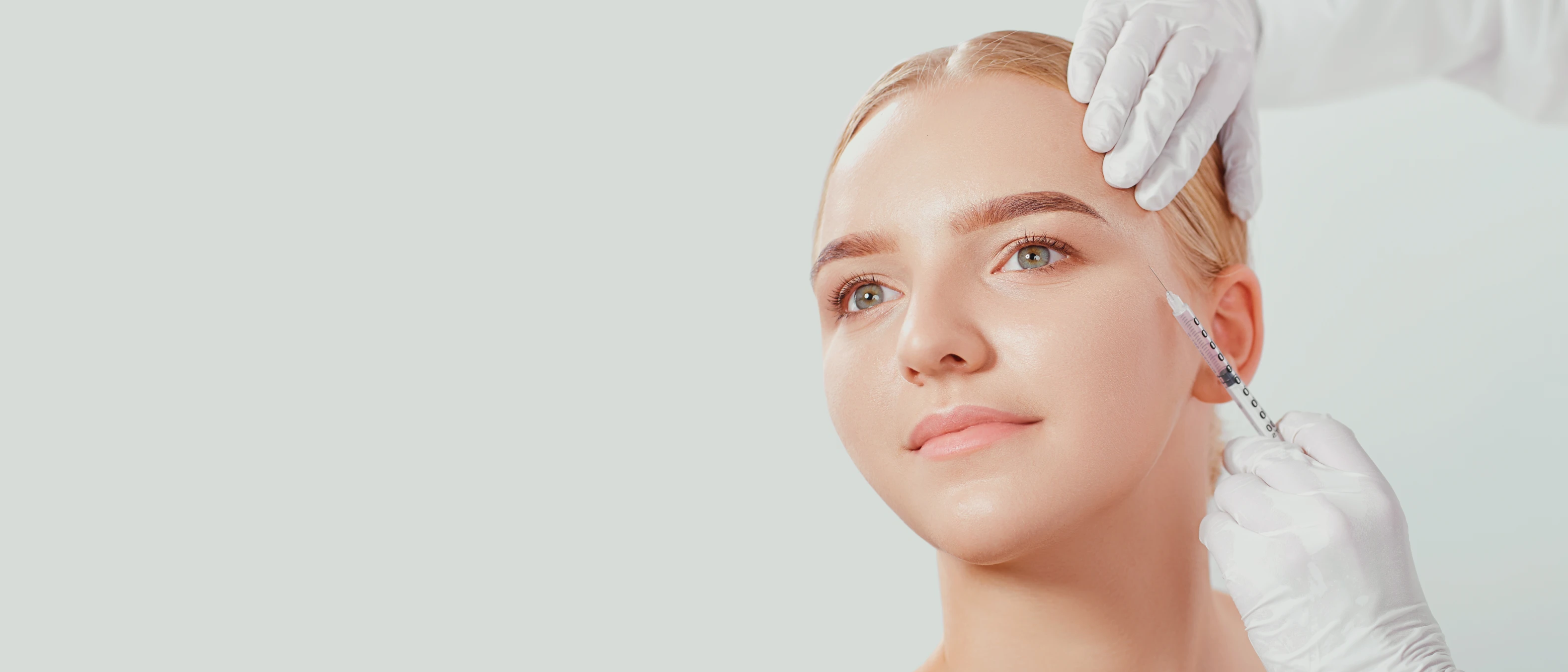 Blonde woman receiving a Botox injection in the Crows Feet area of her eye