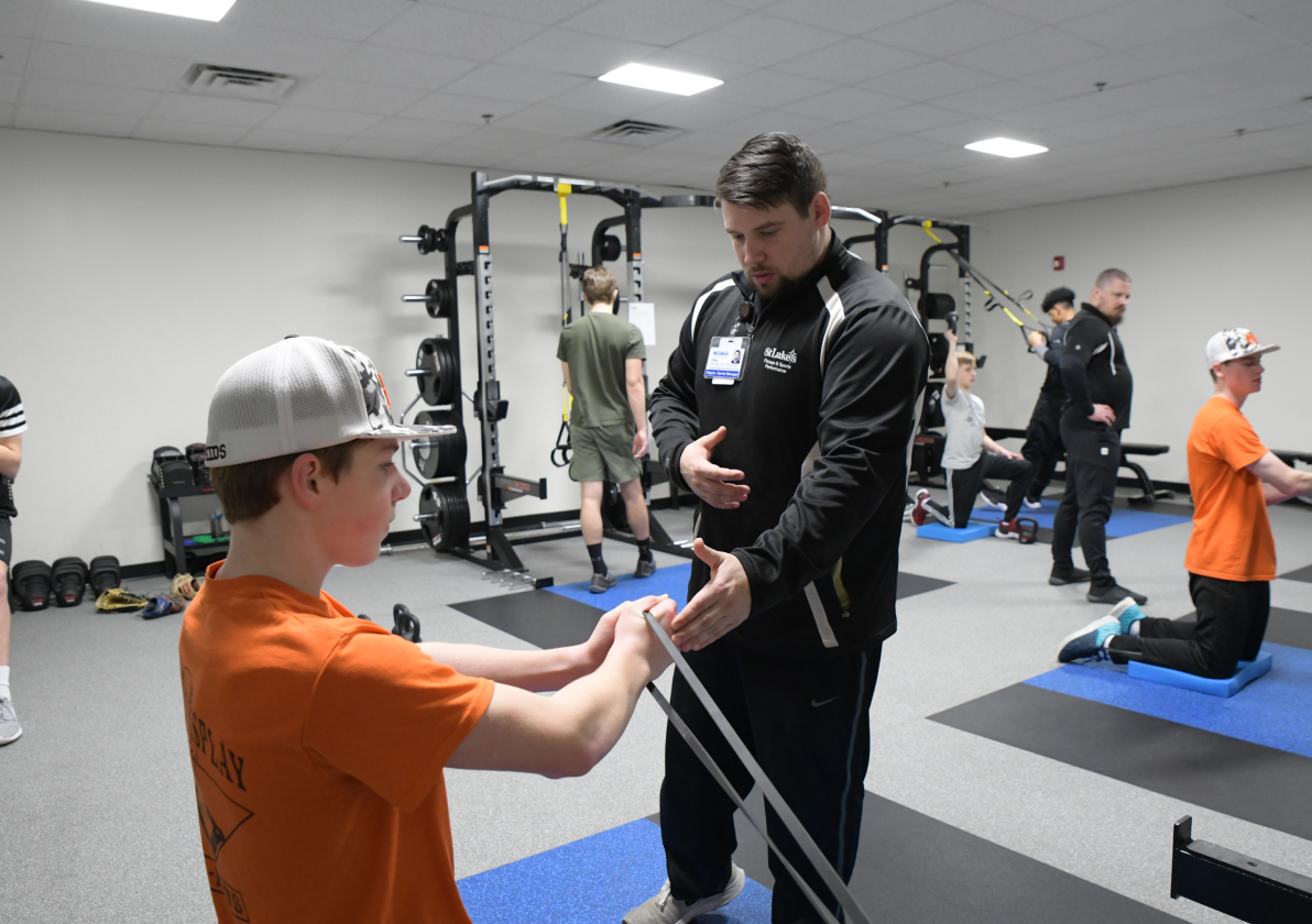 Athletic trainer assisting a young athlete in a weight training room