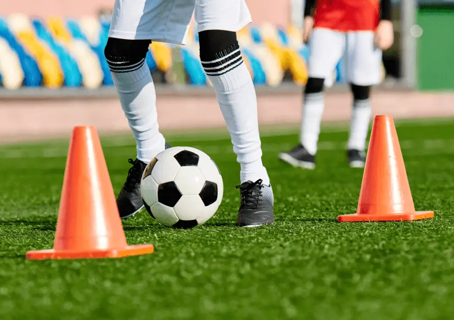 Soccer player dribbling a ball through cones on a field