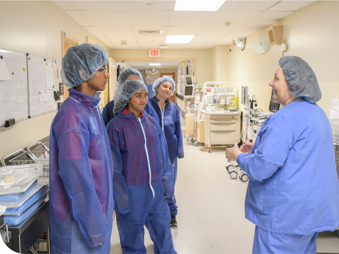 A group of young students in a hospital hallway with a medical professional speaking to them